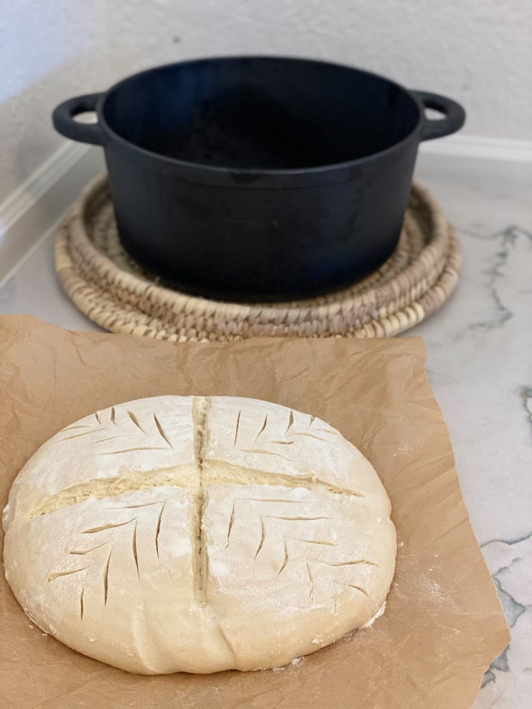 Sourdough bread  scored on parchment paper with a black cast iron Dutch oven in the back 