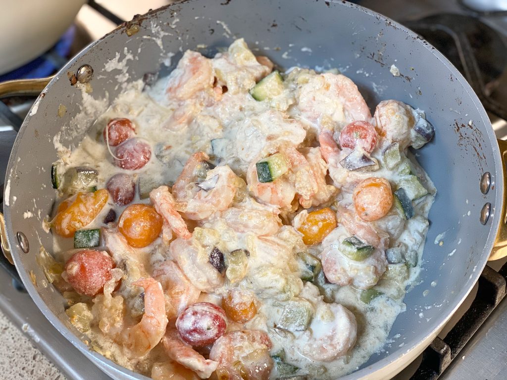 close up shot of shrimp with vegetables in a creamy sauce cooking in a pan