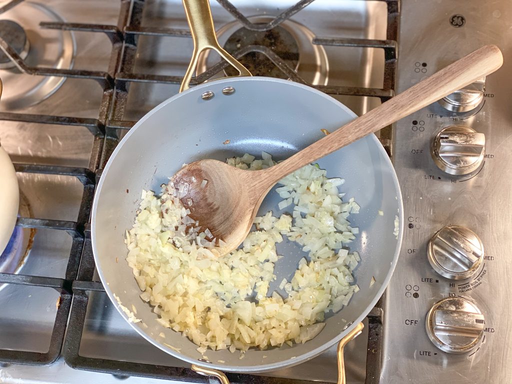 onions sauteing in a pan on a stove with s a wooden stirring spoon