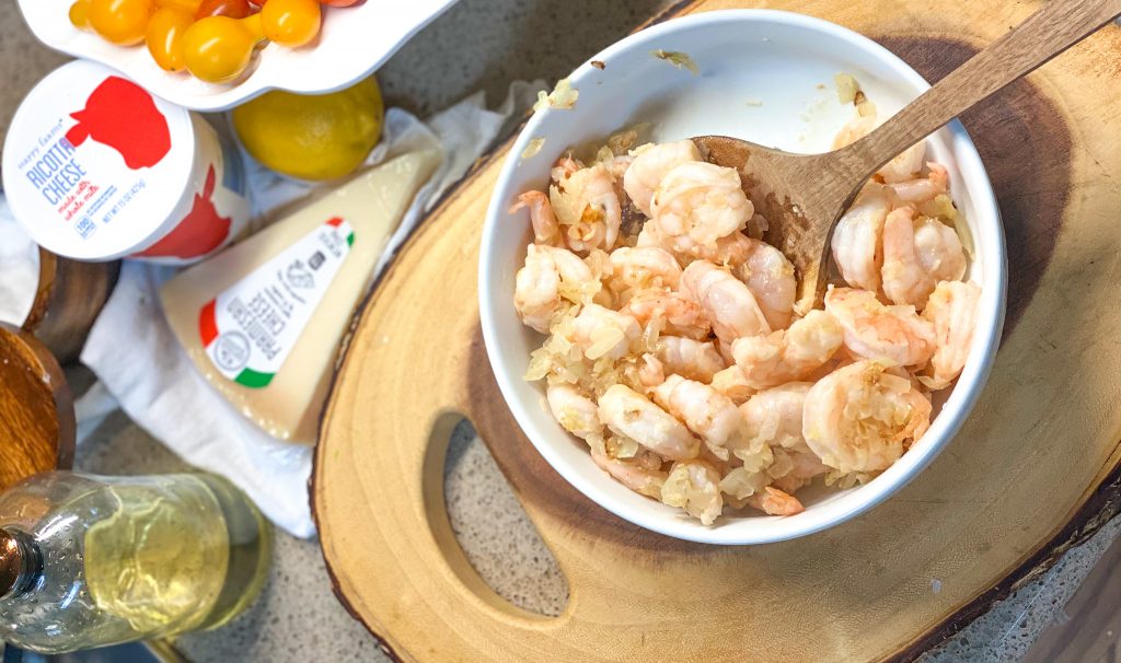 cooked shrimp in a white bowl on a wooden cutting board