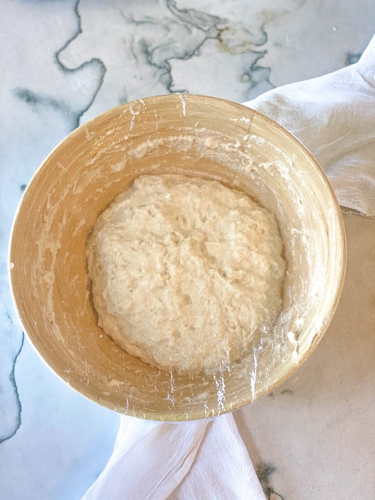 sourdough focaccia dough in a bowl covered with saran wrap
