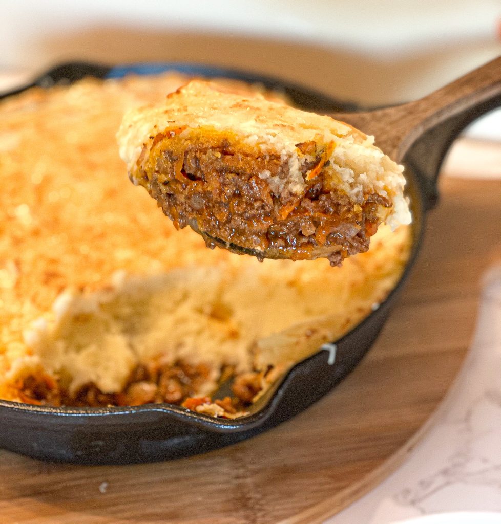 Shepard's pie in a cast iron skillet, with a wooden spoon holding up some pie