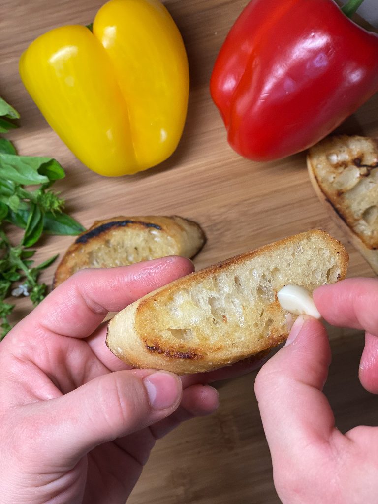 hand rubbing garlic of a toasted baguette slice