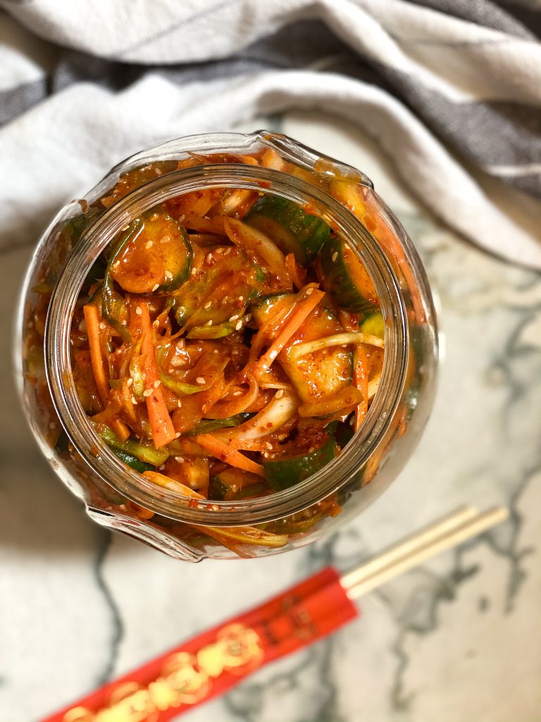 cucumber kimchi in a jar with chopsticks next to it, on a countertop