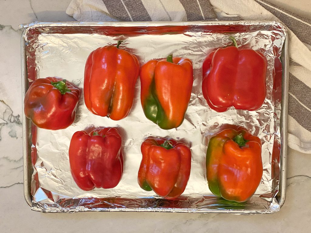 red bell peppers laid out on a baking sheet. Roasted bell peppers