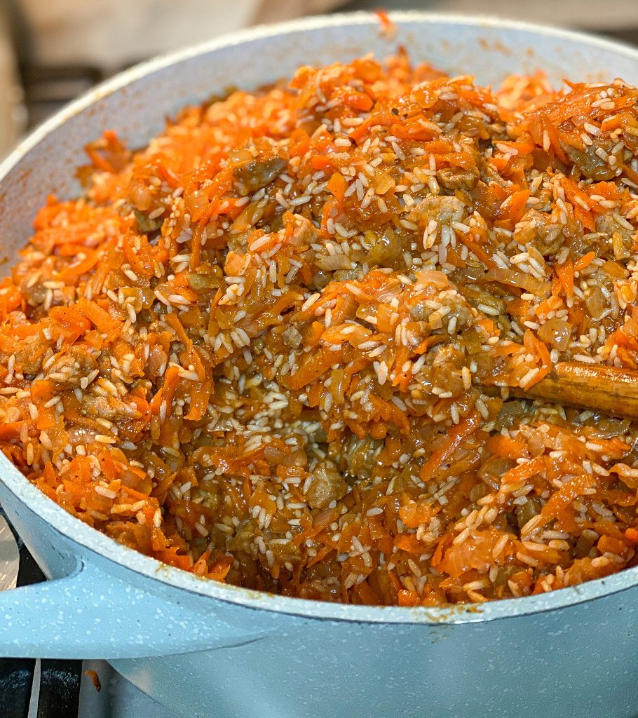 sautéed onion, carrots, meat, and rice in a big blue pot with a wooden spoon