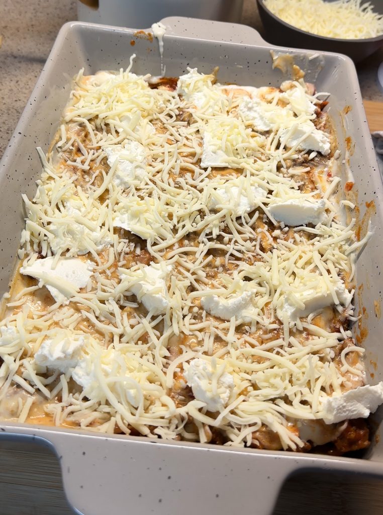 ricotta cheese spooned in top of bechamel sauce with shredded mozzarella cheese for lasagna