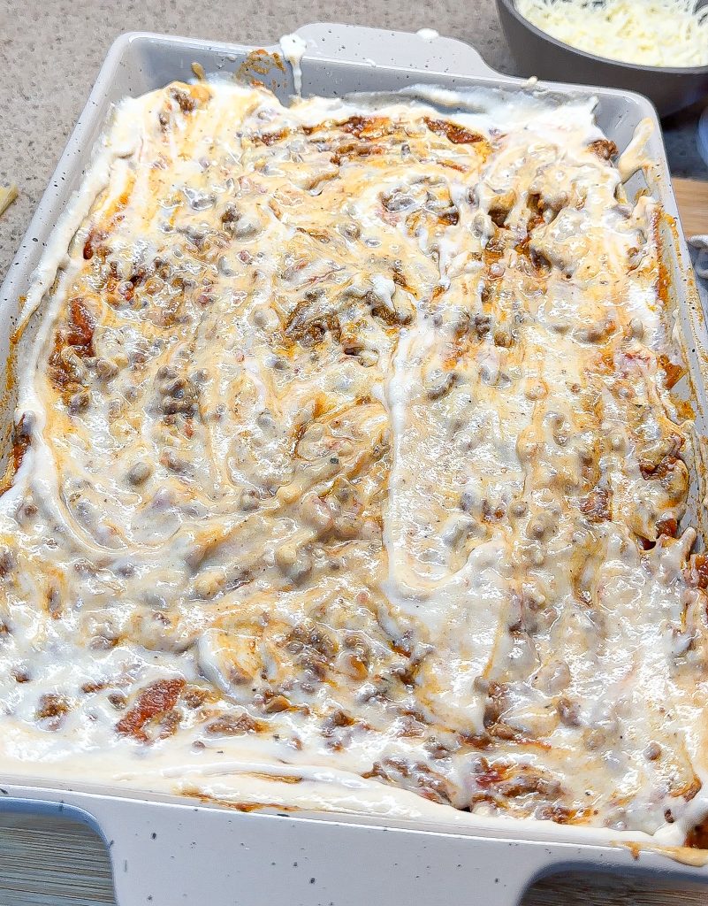 bechamel sauce spread over the meat sauce in a baking dish for lasagna