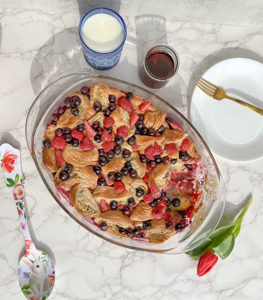 berry croissant bake in a clear dish on a marble tabletop with a floral serving spoon next to it 