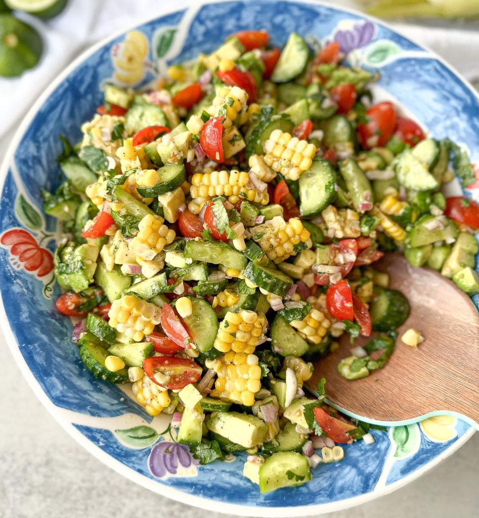 cucumber corn salad in a blue bowl with a big wooden serving spoon