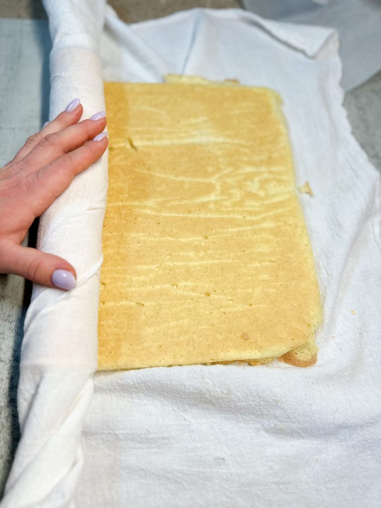 hand rolling a cake into a white tea towel to make a cake roll