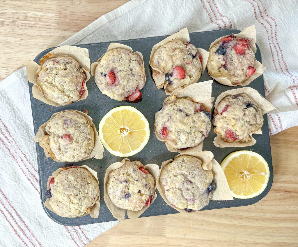 easy lemon ricotta muffins ( with berries) in a muffin tin with a fresh lemon cut in half