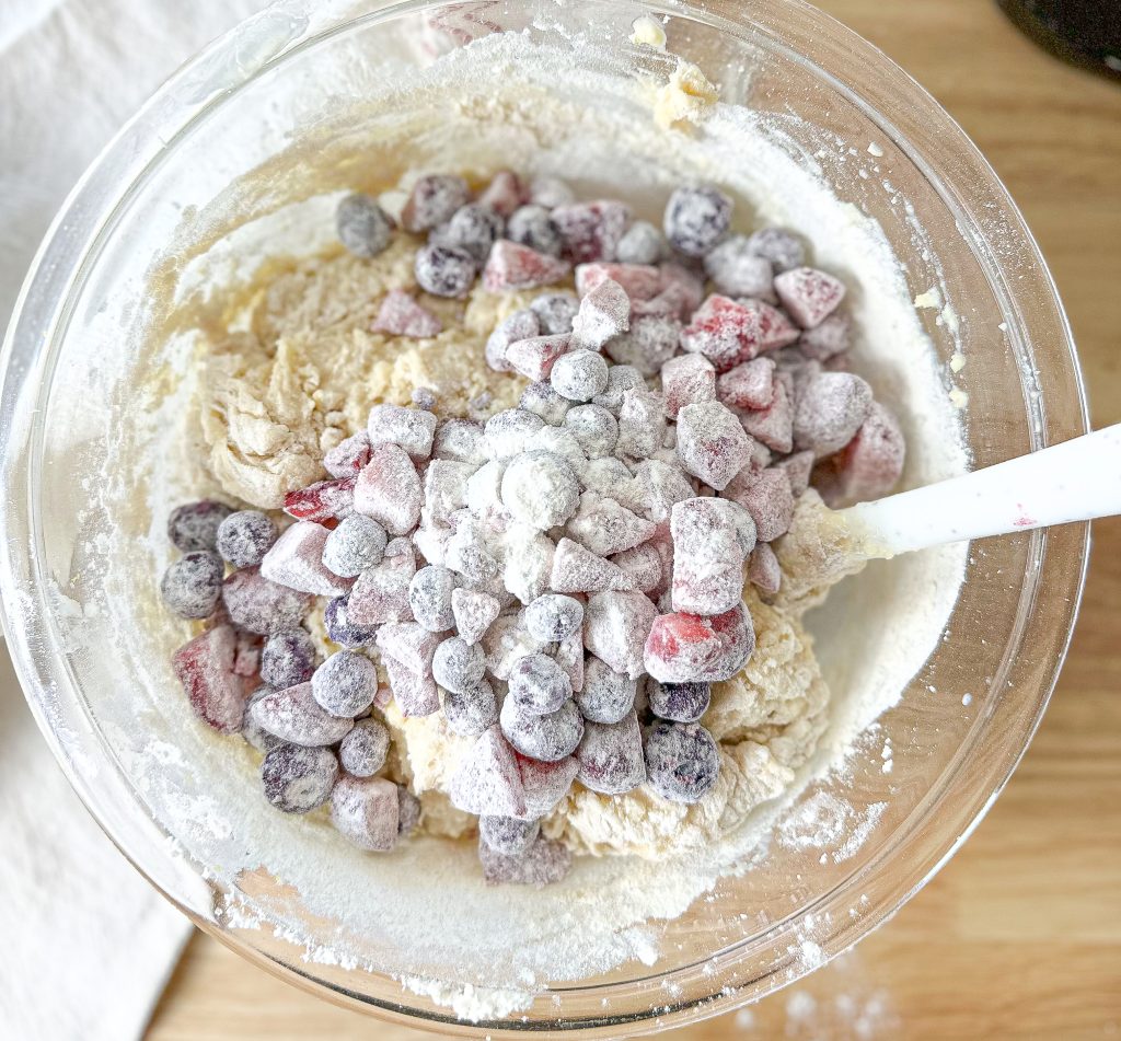 frozen berries dusted in flour that's added to a clear bowl with ricotta batter