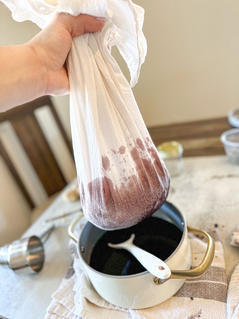 cooked elderberries straining through a cheesecloth over a white pot