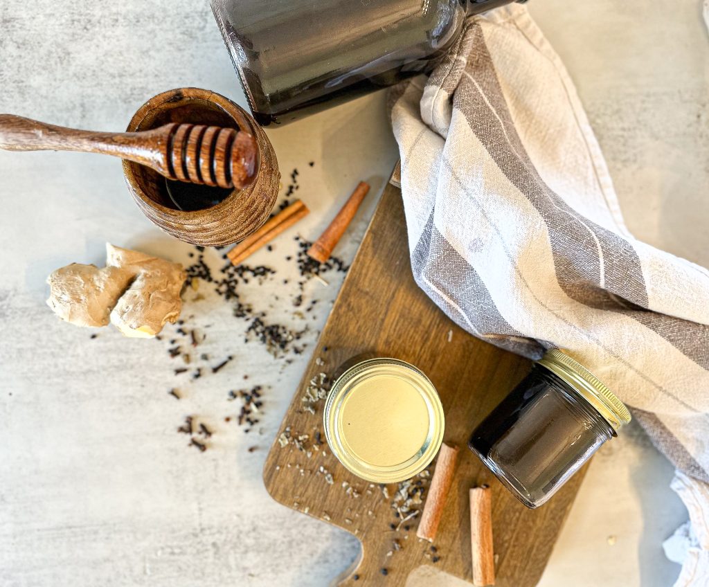 Homemade elderberry syrup (a super cough suppressant) in mason jars and in one big jug on a wooden board with a tea towel next to it on a countertop