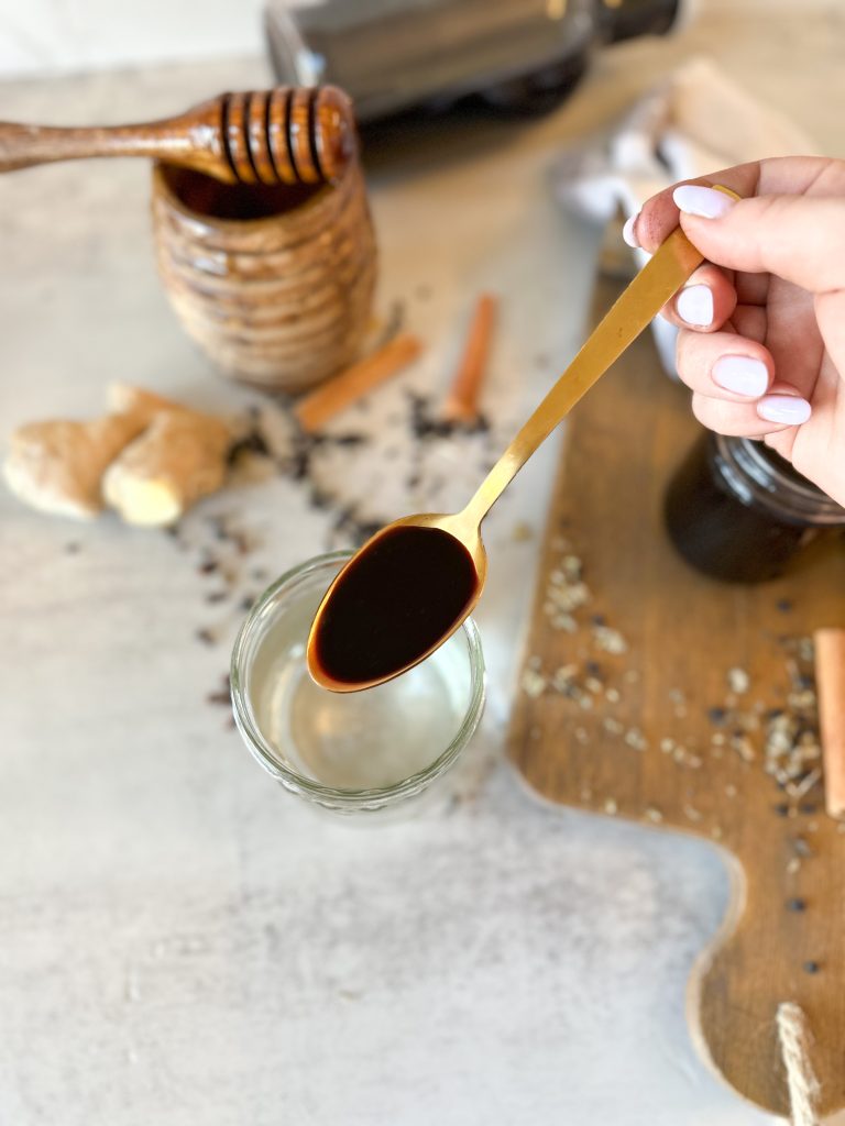 a hand holding a teaspoon of Homemade elderberry syrup (a super cough suppressant) 