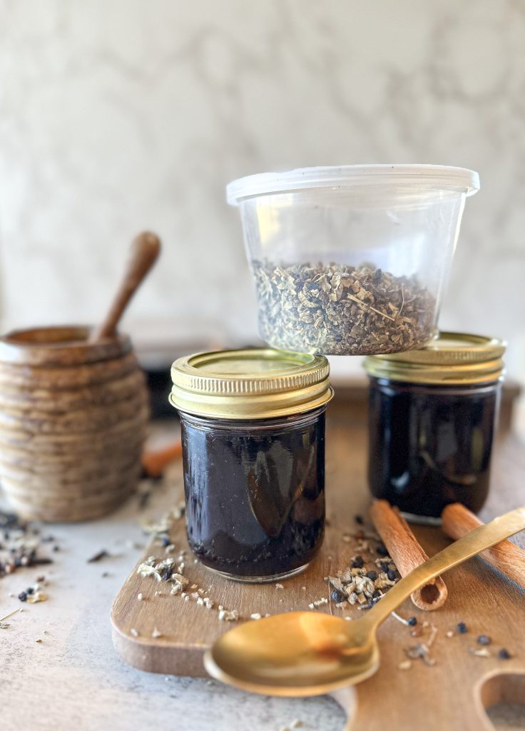 elderberry syrup in small mason jars with a clear plastic tub with dry mullein leaf in it