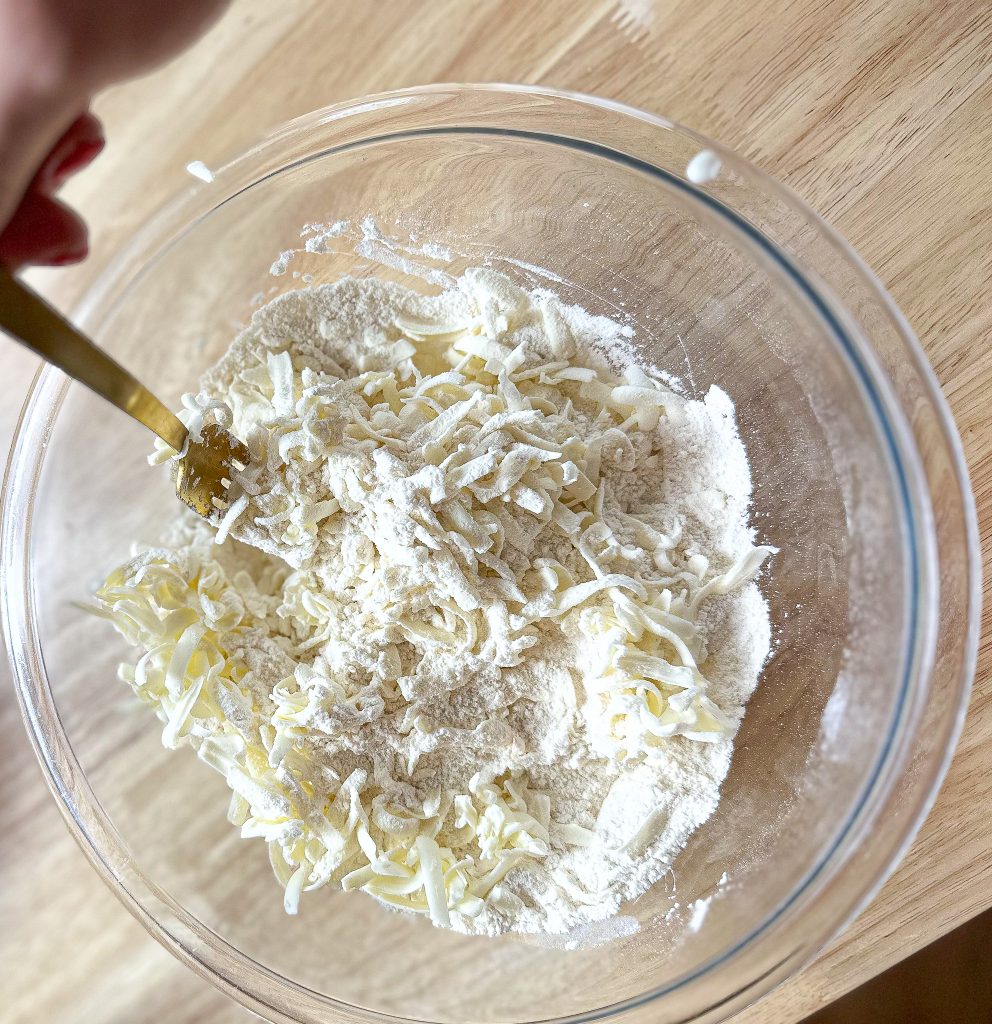hand mixing in grated butter into the flour that's in a clear bowl