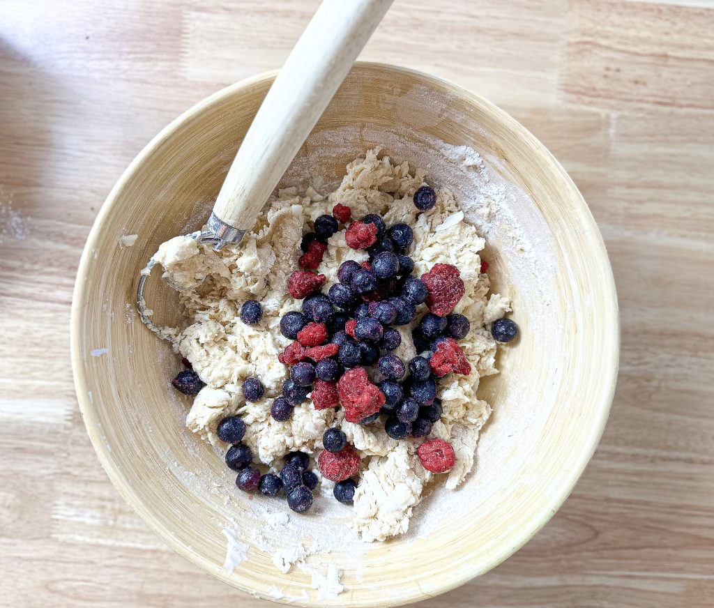 sourdough scone dough in a wooden bowl with frozen raspberries and blueberries 
