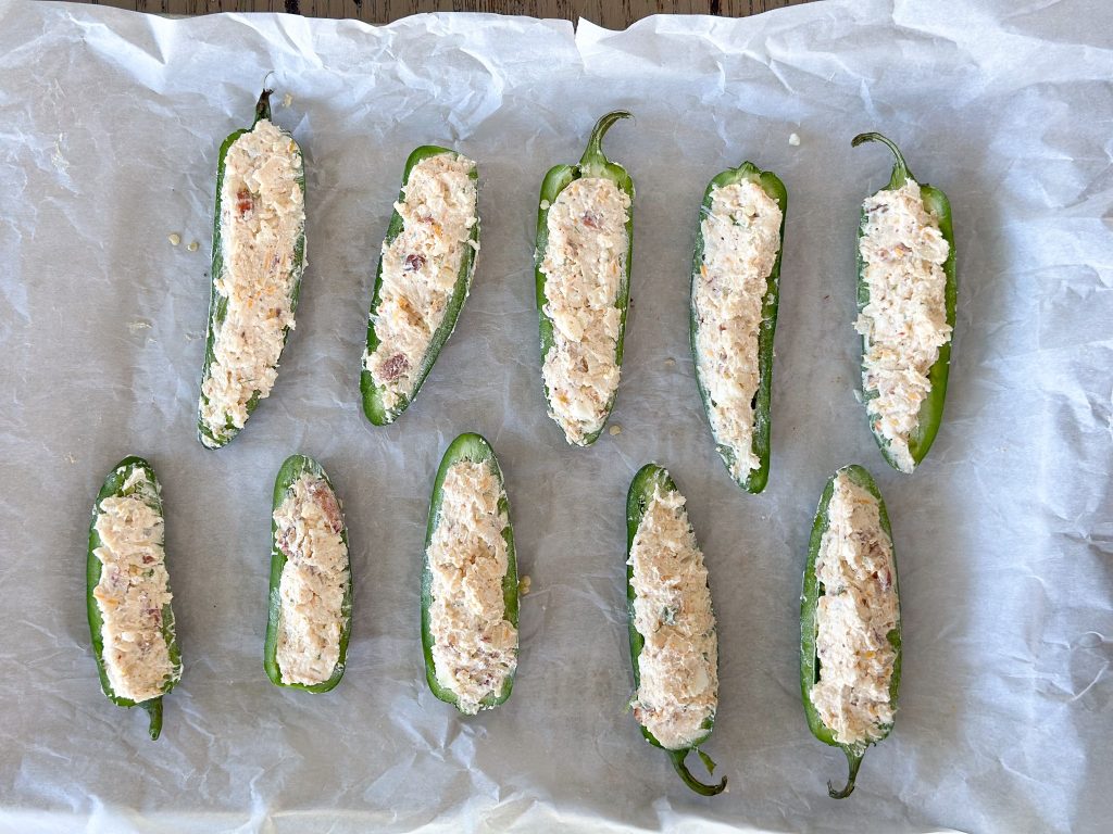 jalapeno peppers stuffed with a creamy Mexican inspired filling with bacon lined on parchment paper on a baking sheet
