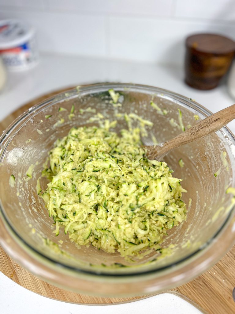 zucchini fritters mixture in a clear bowl with a wooden spoon