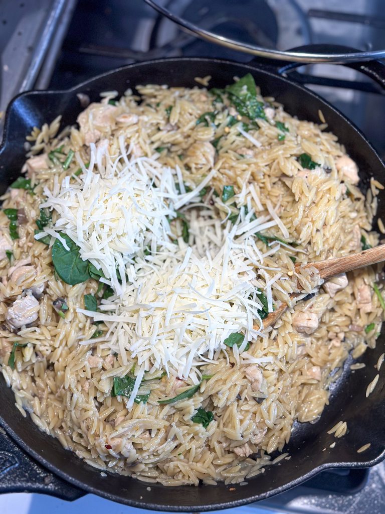 orzo cooking in a cast iron skillet with freshly grated parmesan cheese on top