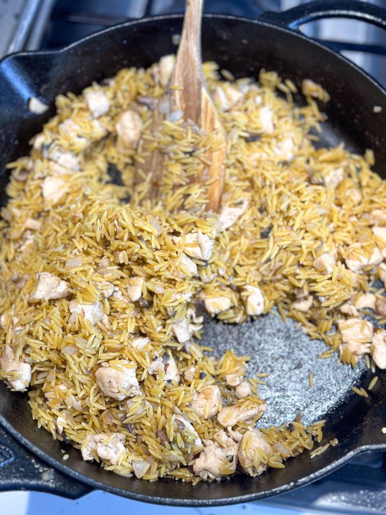 orzo added to toast in a cast iron skillet with butter, chicken, and onions.