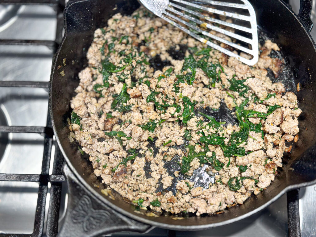 ground pork browning in a cast iron skillet with spinach