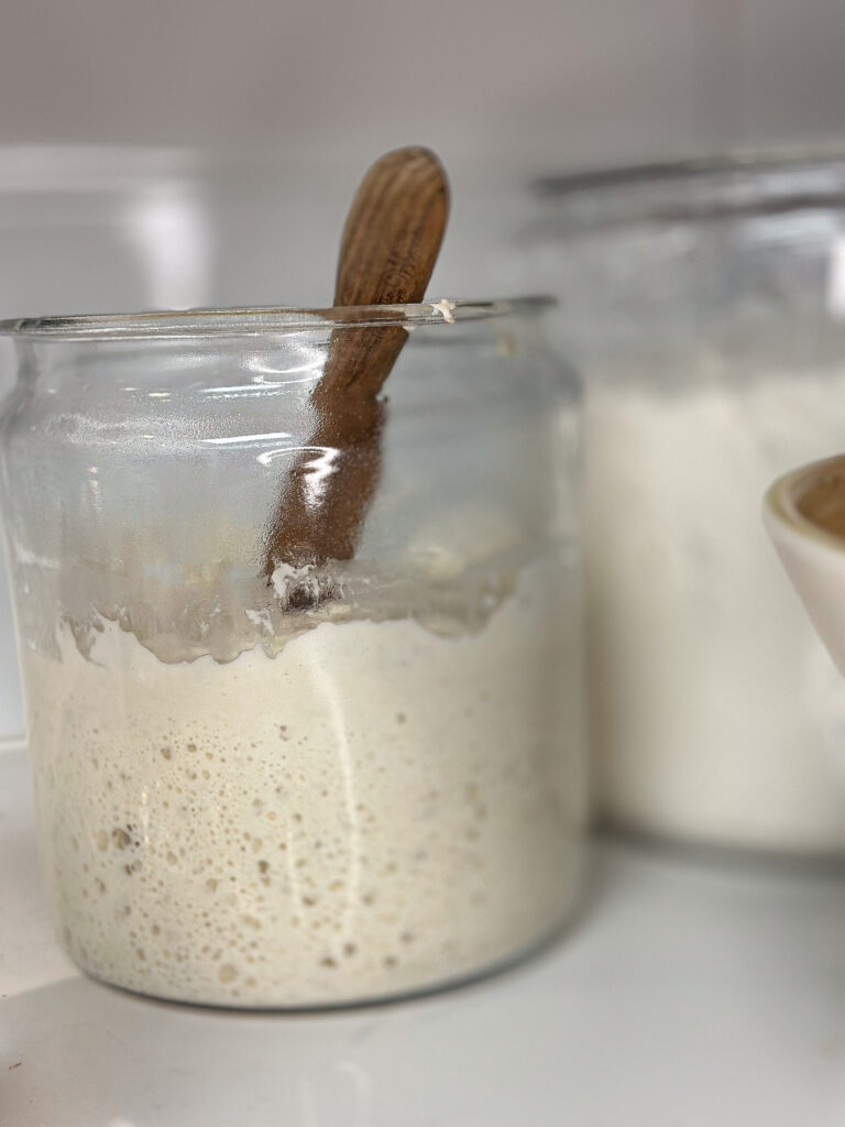leavened sourdough starter in a half gallon jar with a wooden stirring spoon on a quartz countertop
