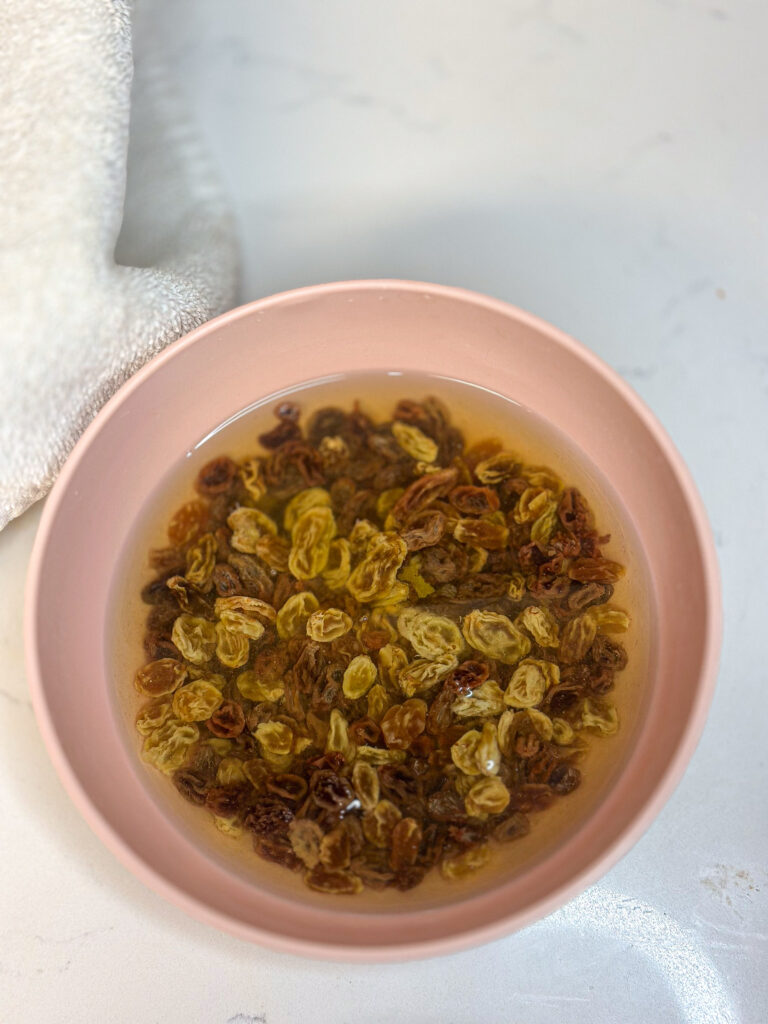 raisins soaking in hot water to rehydrate in a pink bowl