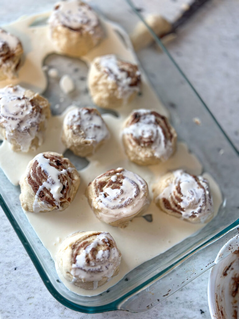 unbaked sourdough cinnamon rolls cut into rolls and placed into a baking tray with drizzled heavy cream on top