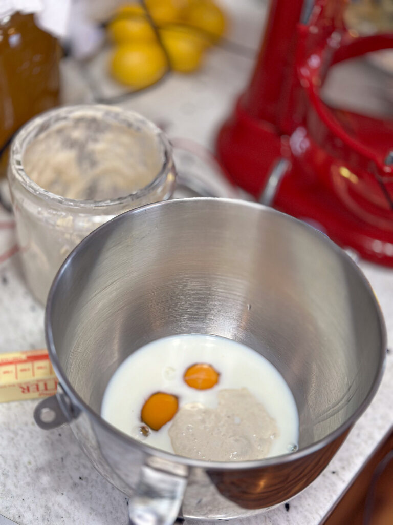 a mixing bowl from the stand mixer is on a granite countertop with liquid ingredients to make sourdough cinnamon rolls.