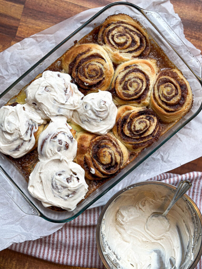 sourdough cinnamon rolls just came out of the oven, baked in a clear baking dish. Half of the cinnamon rolls are frosted with mascarpone frosting