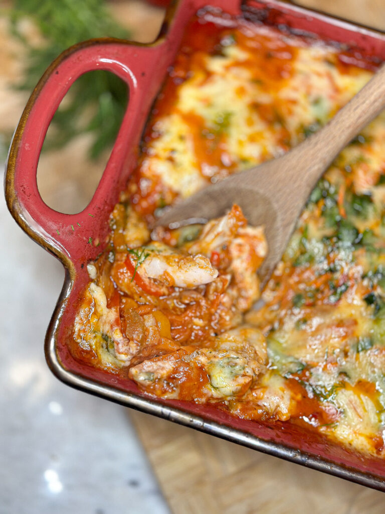 Easy baked white fish with vegetables in a red casserole dish with a wooden spoon scooping out some fish