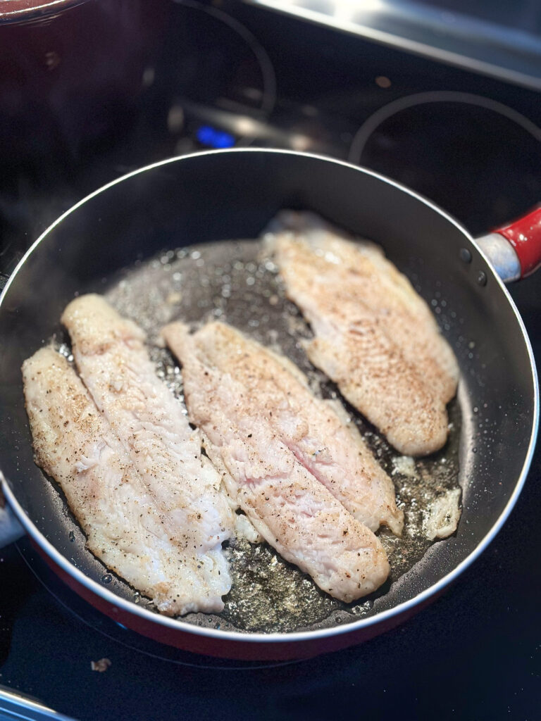 seasoned swai fish sautéing in a black skillet on the stove