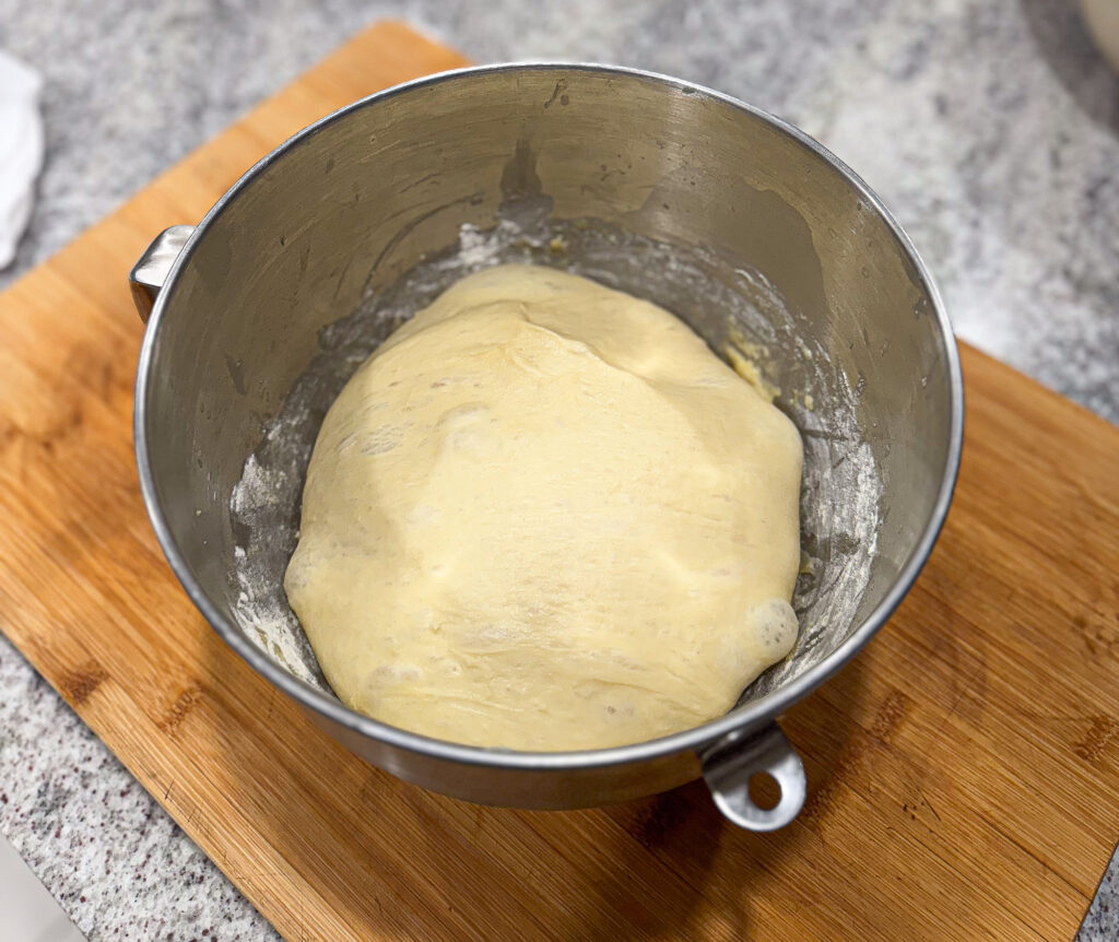 A ball of sourdough kolache dough resting in a metal mixing bowl after bulk fermentation, placed on a wooden board.