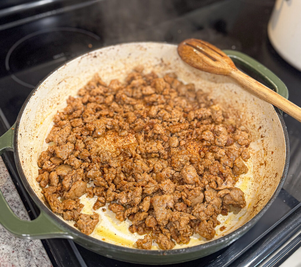 Cooked Italian sausage browning in the same green Dutch oven after roasting the squash, releasing flavor for the creamy butternut squash pasta sauce.