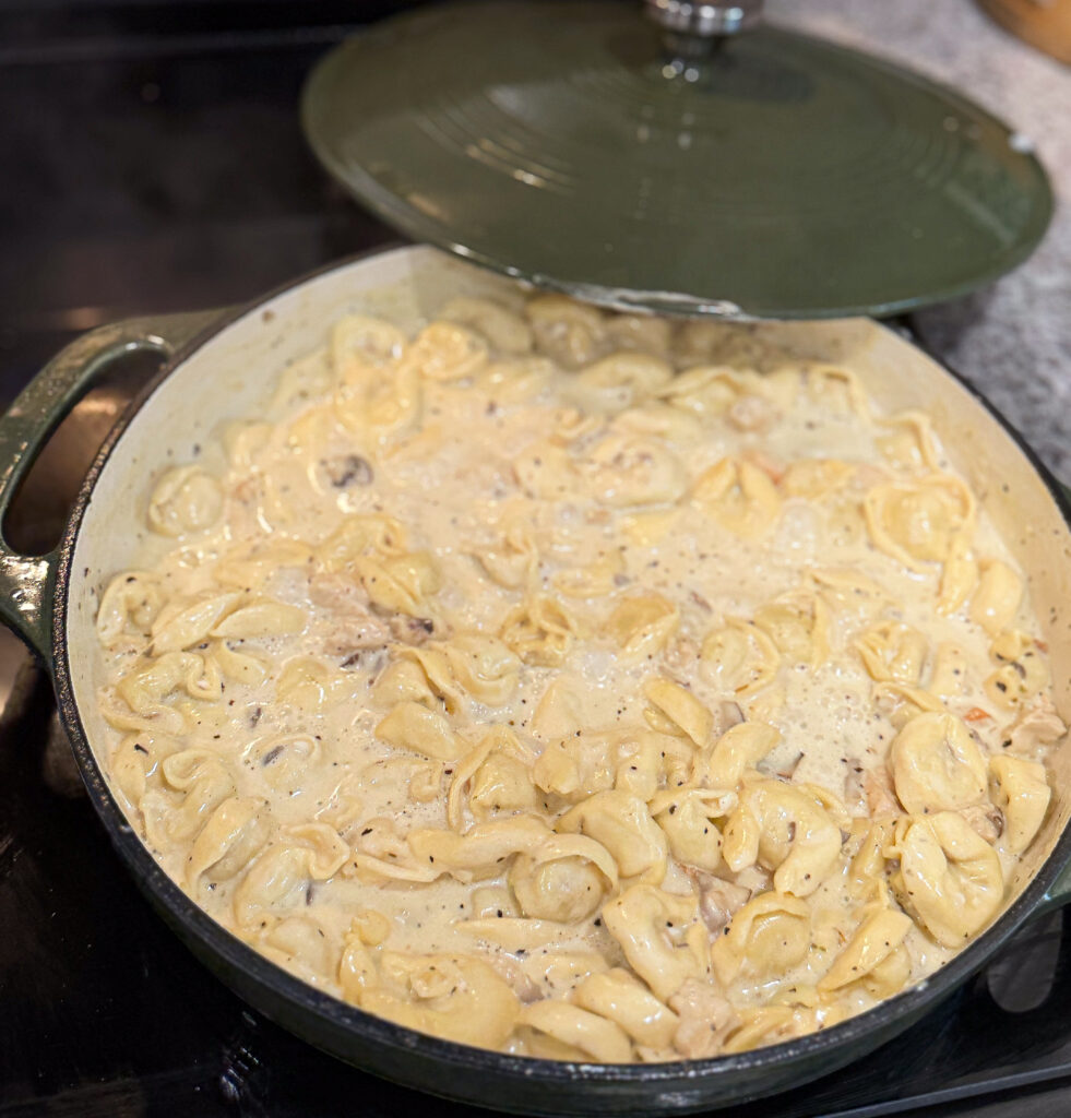 Fresh cheese tortellini added to a creamy Alfredo sauce with chicken and mushrooms in a green Dutch oven.