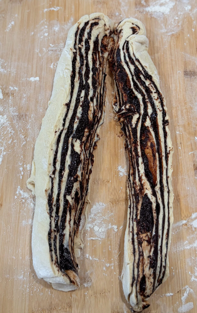 Babka dough log sliced in half lengthwise, showing distinct chocolate swirls and layers before twisting.
