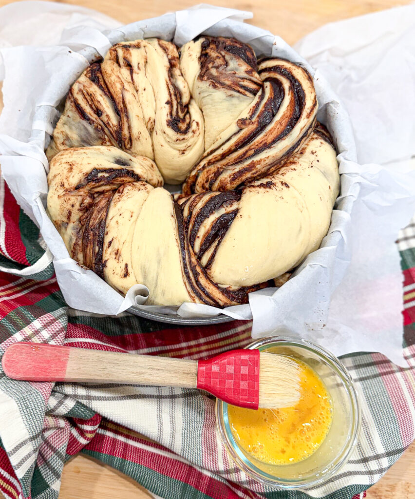 A twisted babka wreath placed in a parchment-lined pan, ready for egg wash and final proofing