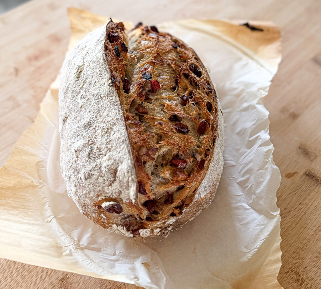 Freshly baked walnut cranberry sourdough loaf on parchment paper, with a golden crust and cranberries peeking through the scored top.