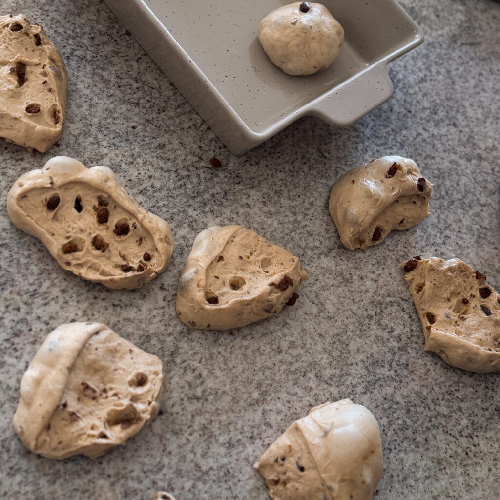 Portioned sourdough hot cross bun dough cut into equal pieces with visible dried fruit throughout