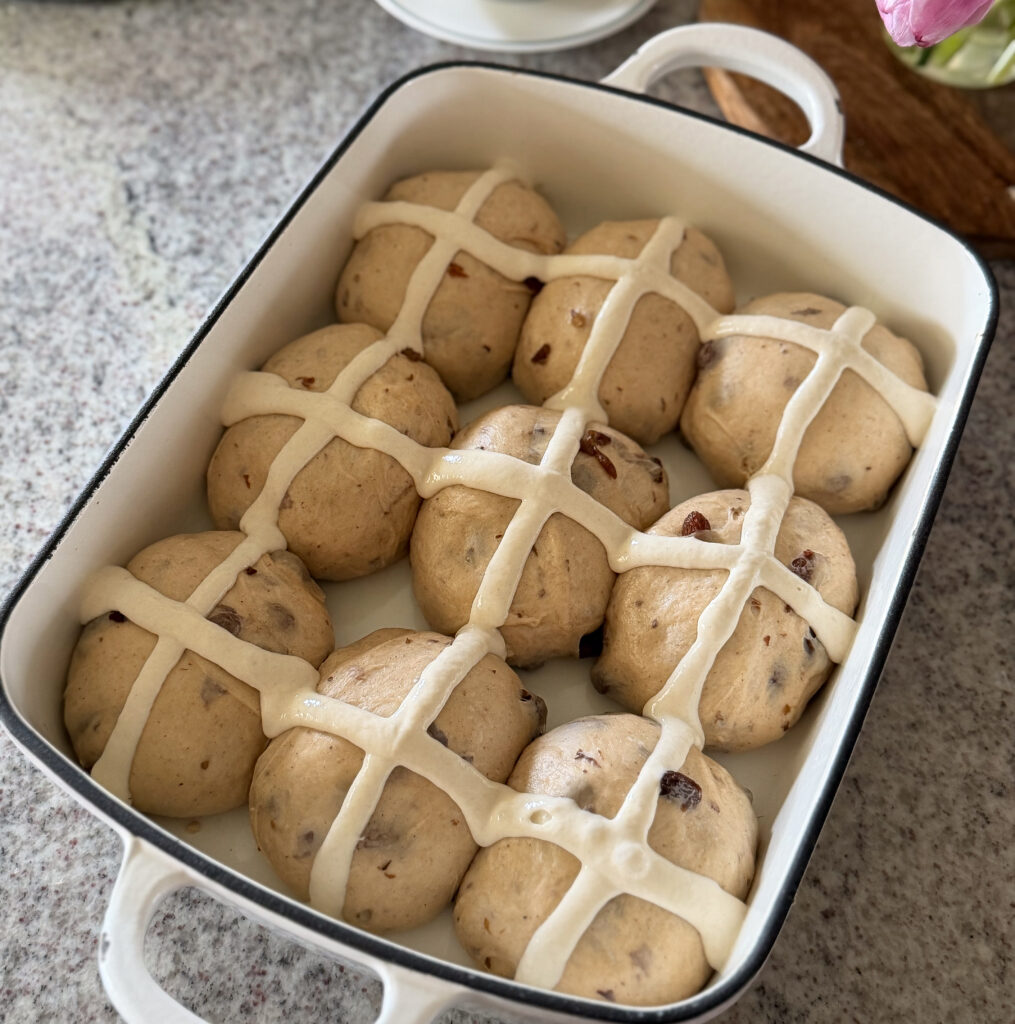 Sourdough hot cross buns after final proof with flour paste crosses piped on top, ready to bake in a ceramic baking dish