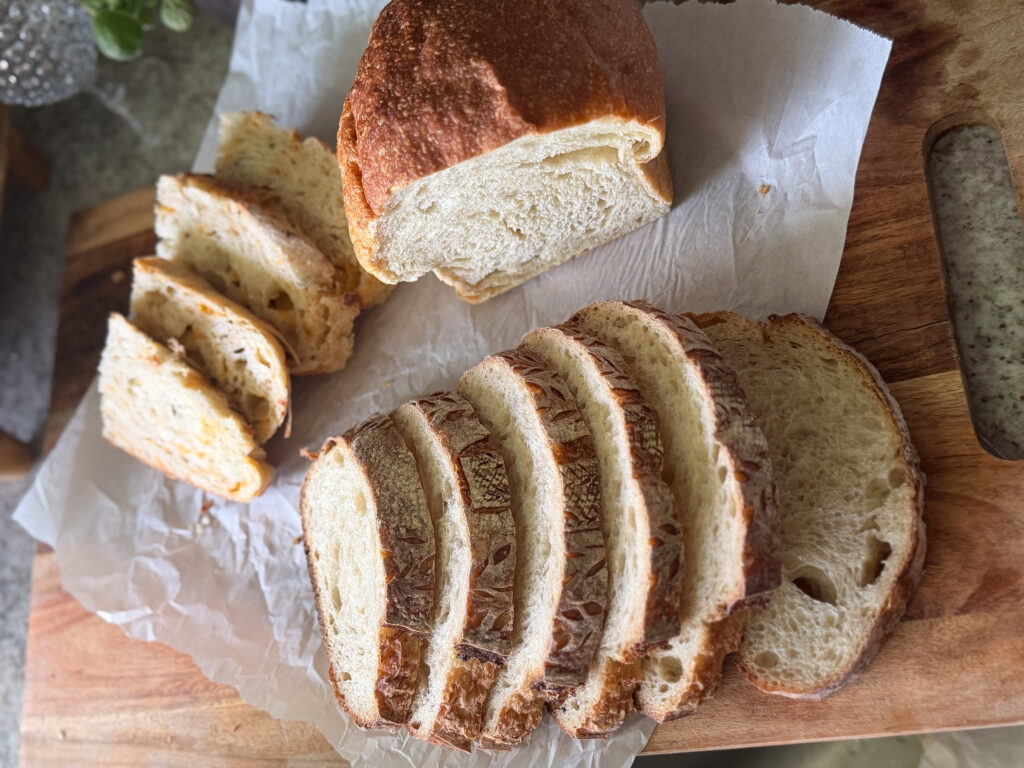 Different types of sliced sourdough breead on a cutting board, cheddar jalepeno, classic sourdough loaf, and croissant loaf