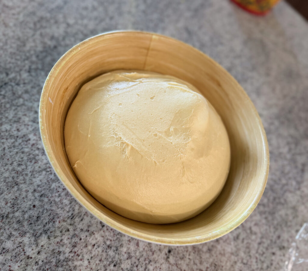 A bowl of risen dough sits on a gray countertop, ready for the next step in baking.