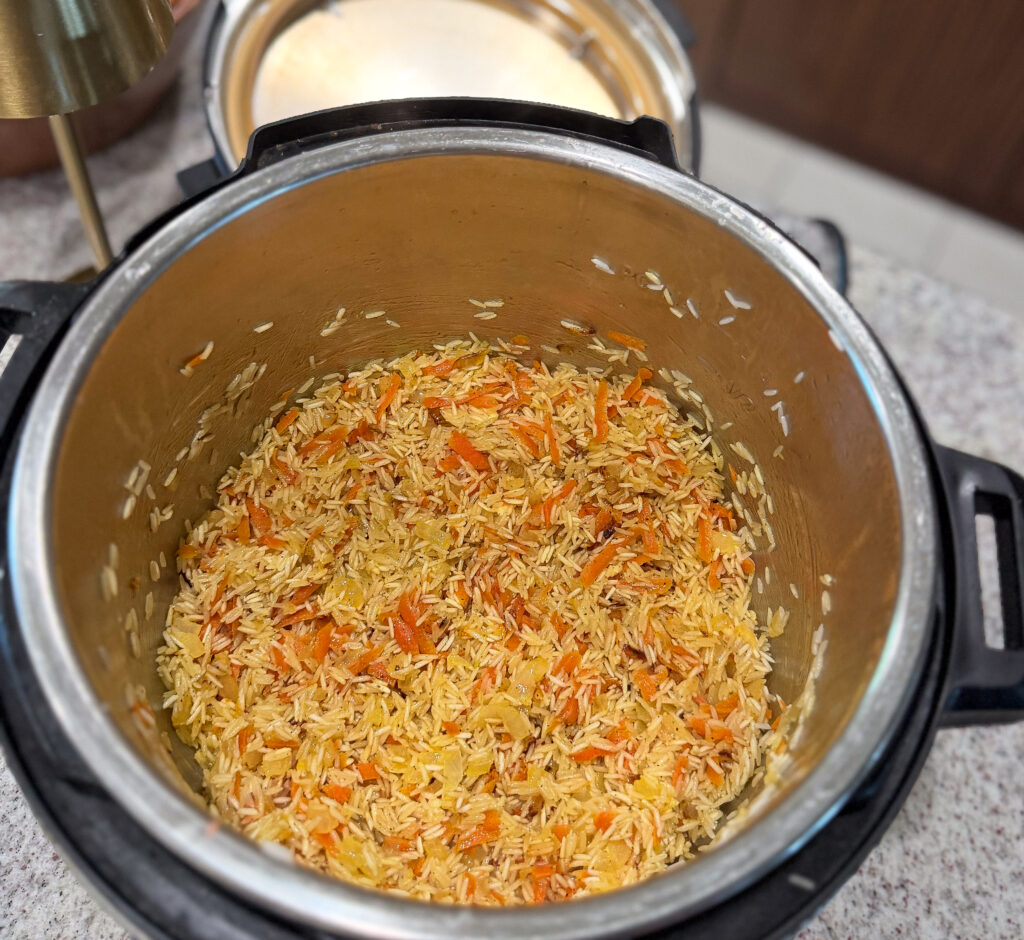 An electric pressure cooker filled with uncooked rice mixed with shredded carrots, placed on a kitchen countertop.