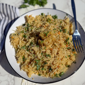A plate of seasoned rice garnished with chopped herbs and a whole roasted garlic bulb, with a fork resting on the side of the plate.