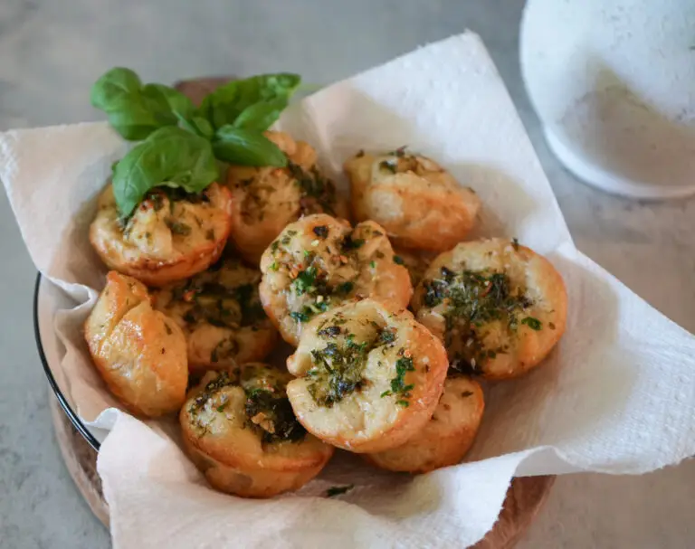 A bowl lined with paper towels holds several baked savory pastries topped with herbs, garnished with fresh basil leaves.