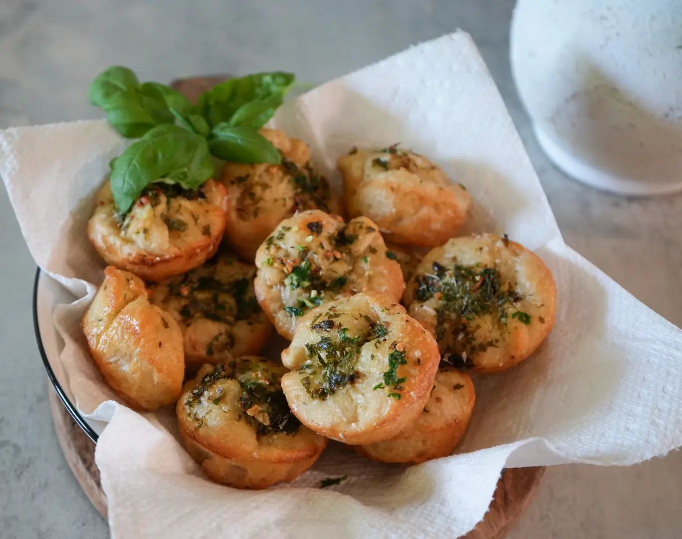 A bowl lined with paper towels holds several baked savory pastries topped with herbs, garnished with fresh basil leaves.