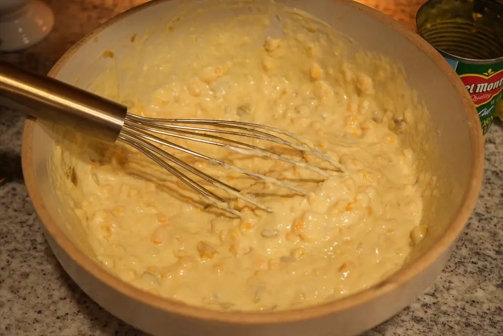 A metal whisk in a bowl of creamy corn batter.